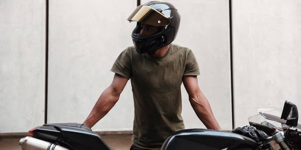 a Boise motorcycle rider standing and leaning over his bike with a helmet on